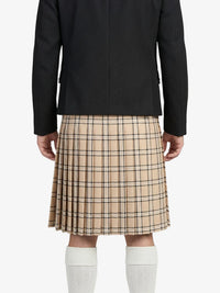 Person wearing a black coat and beige plaid kilt on a white background