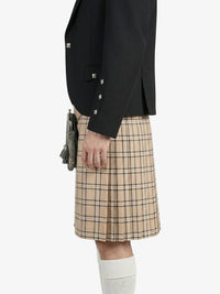 Person wearing a black blazer and beige plaid kilt on a white background