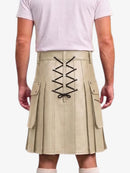 A beige pleated kilt with black lace-up detailing on the back, shown on a model wearing a light pink t-shirt against a white background.