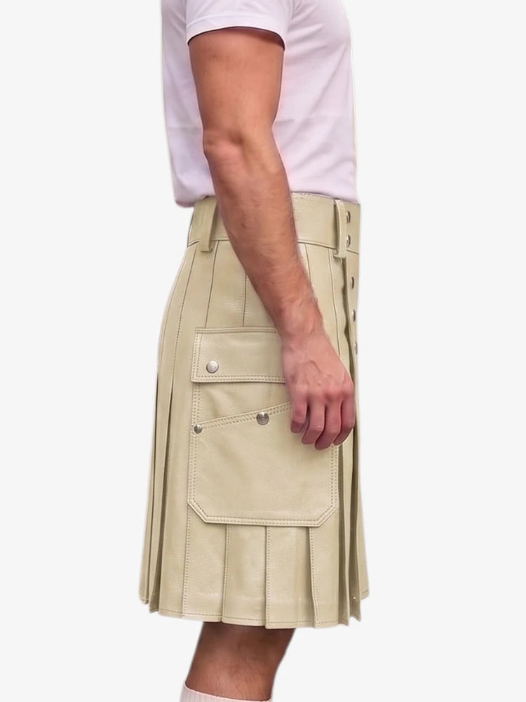 A side view of a person wearing a beige faux-leather kilt with pleats, flap pockets, and decorative metal studs, paired with a light pink t-shirt against a plain white background.