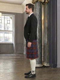 Man wearing a black jacket and red plaid kilt in an elegant interior setting.