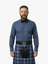 Man wearing a blue shirt, bow tie, and tartan kilt on a white background