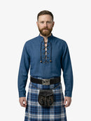 Man wearing a blue shirt with lace-up front and a plaid kilt on a white background