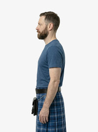 Man wearing a blue t-shirt and plaid skirt standing against a white background