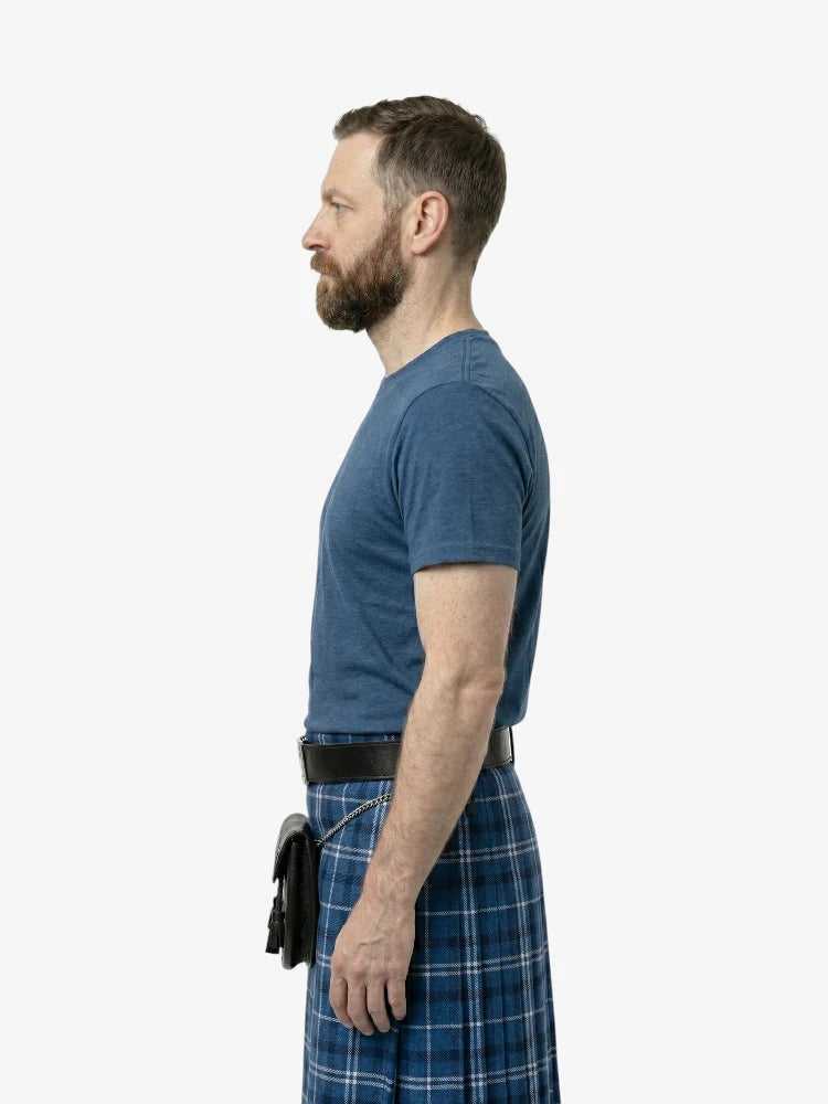 Man wearing a blue t-shirt and plaid skirt standing against a white background