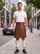 A man stands on a city sidewalk wearing a brown leather kilt, a white t-shirt, white knee-high socks, and black leather shoes. The background shows a blurred street scene with buildings, trees, a parked black car, and a bicycle.