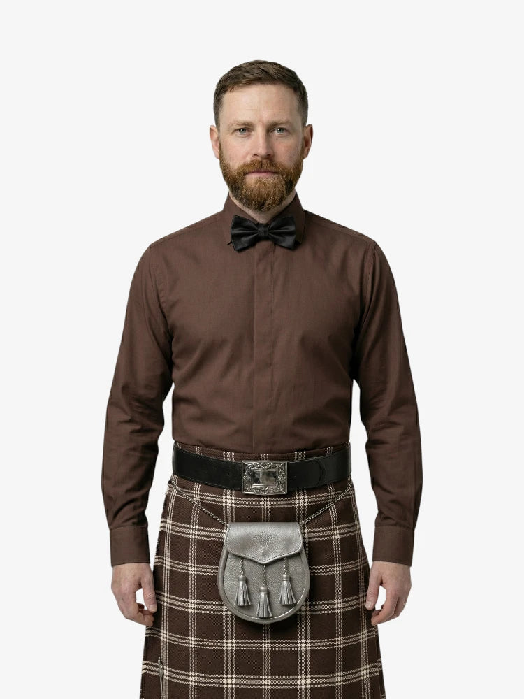 Man wearing a brown shirt, bow tie, and tartan kilt on a white background