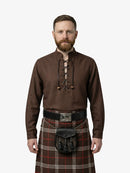 Man wearing a brown shirt with lace-up front and a tartan kilt on a white background