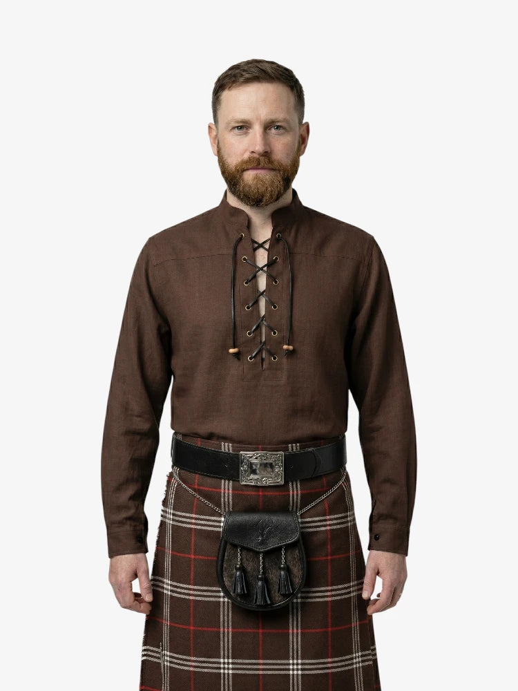 Man wearing a brown shirt with lace-up front and a tartan kilt on a white background