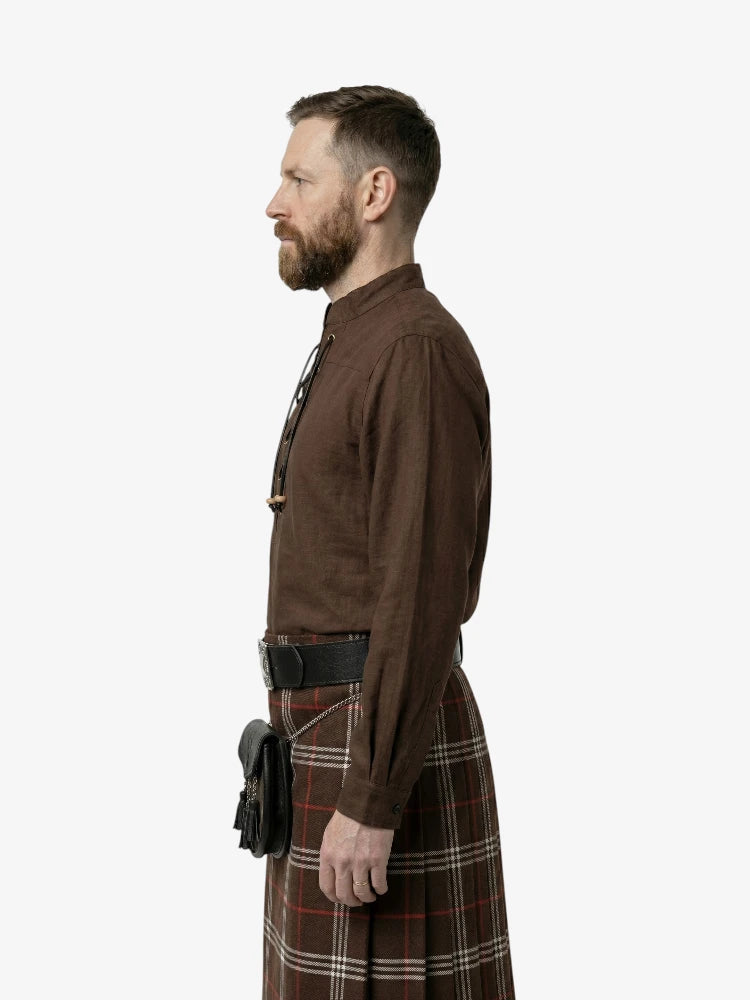 Man wearing a brown shirt and tartan kilt on a white background