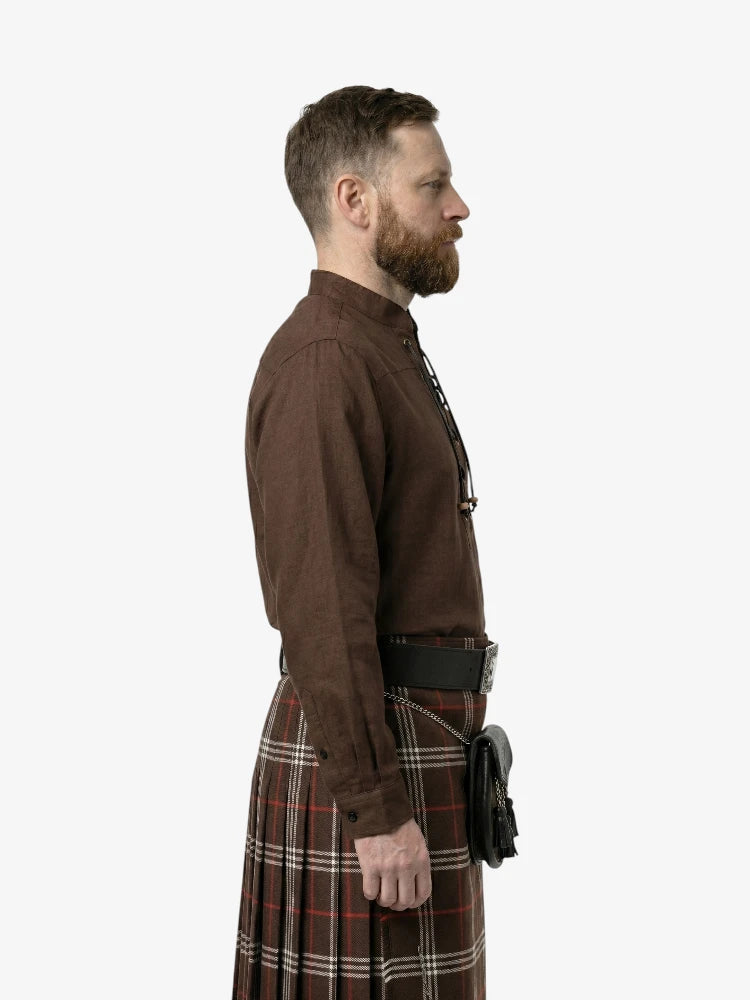 Man wearing a brown shirt and plaid kilt on a white background