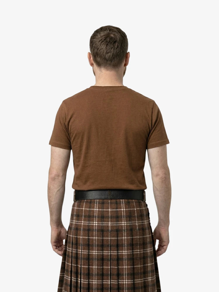 Man wearing a brown t-shirt and plaid kilt on a white background