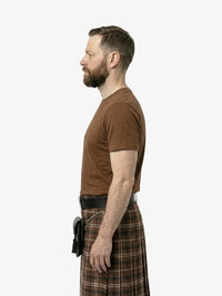 Man wearing a brown t-shirt and plaid kilt on a white background