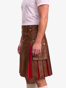 A man wearing a brown faux-leather kilt with pleated red fabric lining and silver hardware, paired with a white t-shirt and white socks, shown from the waist down against a light gray background.