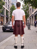 A man viewed from behind wearing a dark brown leather kilt with lace-up back detailing, a white t-shirt, and white knee-high socks, standing on a city sidewalk.
