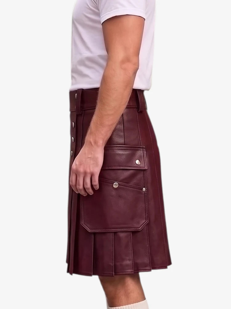 A man wearing a burgundy faux-leather kilt with silver snap button details and pleated front pockets, paired with a white t-shirt, shown from the side against a light gray background.