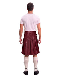A man shown from the back wearing a burgundy pleated kilt, a light pink t-shirt, cream knee-high socks, and black shoes, isolated on a white background.