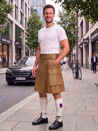 A man stands on a city sidewalk wearing a tan leather kilt with multiple flap pockets, a white t-shirt, white knee-high socks, and black leather shoes. A black Mercedes-Benz car is parked on the street behind him, with storefronts and trees in the background.