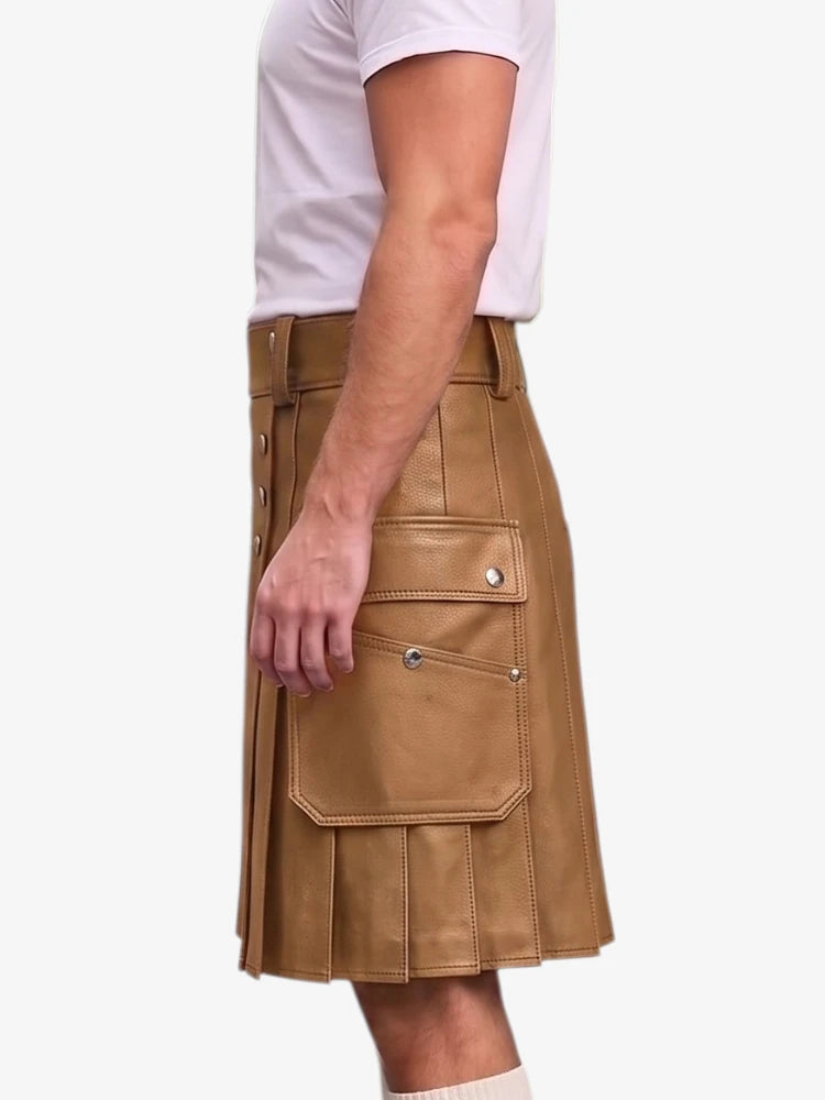 A side view of a person wearing a tan faux-leather kilt with flap pockets and silver snap details, paired with a white t-shirt and white socks, against a light gray background.