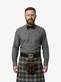 Man wearing a gray shirt, bow tie, and plaid kilt on a white background