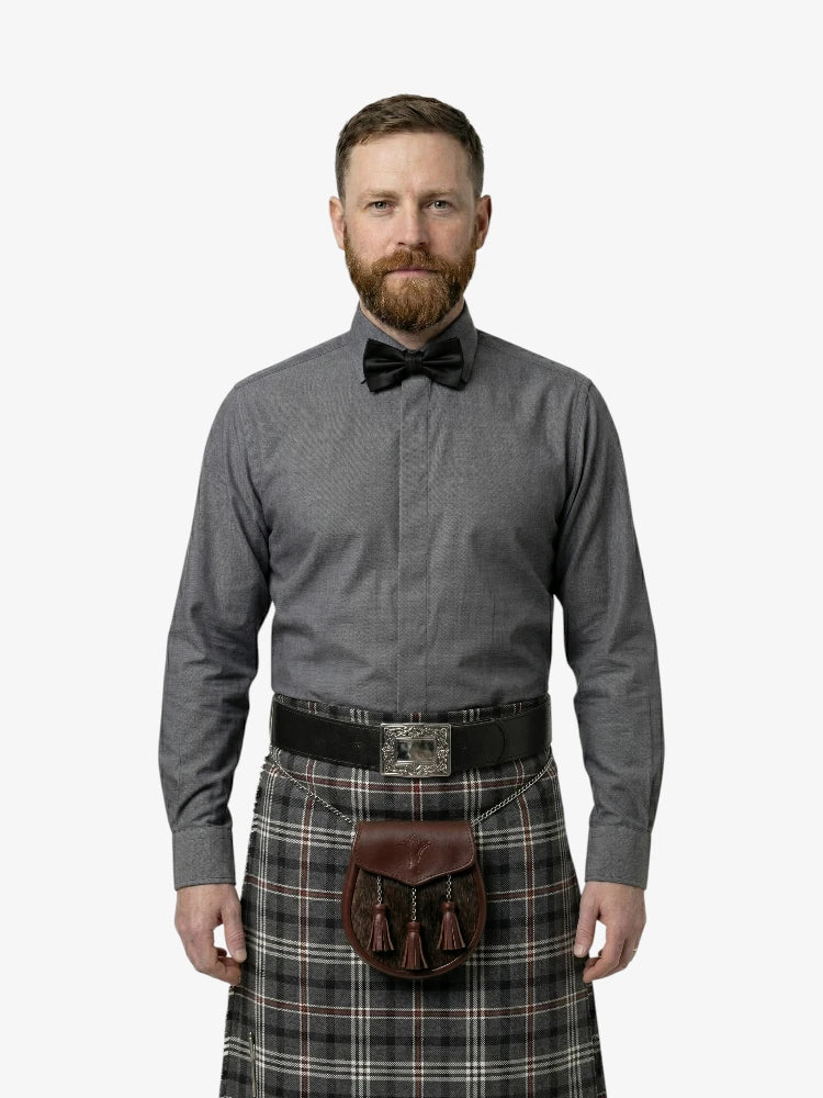 Man wearing a gray shirt, bow tie, and plaid kilt on a white background
