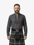 Man wearing a dark gray shirt with lace-up front and a plaid kilt on a white background