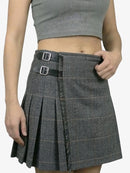 Person wearing a gray pleated skirt with a plain background