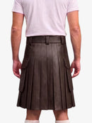 A person shown from the back wearing a dark brown pleated leather kilt with side cargo pockets, paired with a light pink t-shirt and white socks, against a plain light gray background.