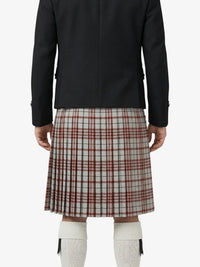 Person wearing a black jacket and plaid kilt on a white background