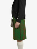 Person wearing a black jacket and green plaid kilt on a white background