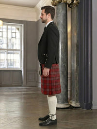 Man wearing a black jacket, red plaid kilt, and white stockings in an elegant room.