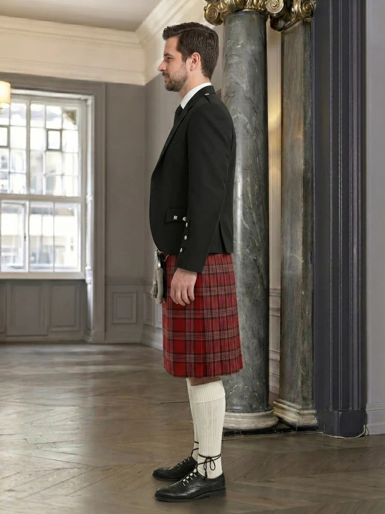 Man wearing a black jacket, red plaid kilt, and white stockings in an elegant room.