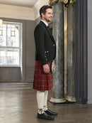 Man wearing a black jacket and red plaid kilt in an elegant interior setting.