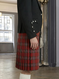 Person wearing a black blazer and red plaid kilt indoors.