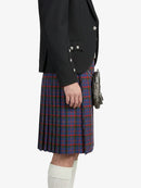 Person wearing a black blazer with studded details and a red and blue plaid kilt on a white background