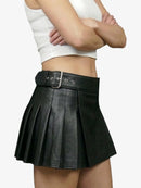 Person wearing a black pleated skirt with a white top on a plain background