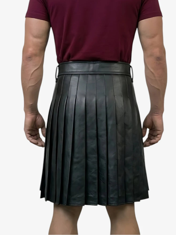 Person wearing a black pleated leather skirt with a plain background