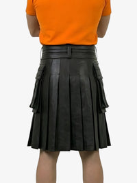 Person wearing an orange shirt and black pleated leather skirt on a white background