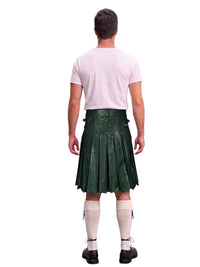 A man shown from the back wearing a dark green pleated kilt, a light pink t-shirt, cream knee-high socks, and black shoes, isolated on a white background.