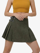 Person wearing a green pleated skirt with black buckles on a white background