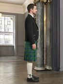 Man wearing a black jacket and green plaid kilt in an elegant interior setting.