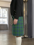 Person wearing a black jacket and green plaid kilt in an indoor setting.