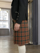 Person wearing a black jacket and plaid kilt indoors.