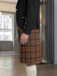 Person wearing a black jacket and plaid kilt indoors.