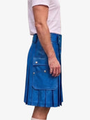 A person wearing a bright blue pleated leather kilt with front flap pockets and silver snap buttons, paired with a light pink t-shirt, shown from the side against a plain white background.