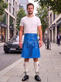 A man standing on a city sidewalk wearing a bright blue leather kilt with a white t-shirt, white knee-high socks, and black leather shoes. The background shows a street scene with buildings, a parked black Mercedes, and a bicycle.