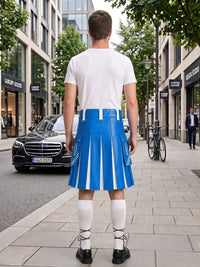 A man stands on a city sidewalk facing away from the camera, wearing a white T-shirt and a bright blue pleated kilt with white vertical stripes, white knee-high socks, and black shoes. Buildings, trees, a black car, and a bicycle are visible in the background.