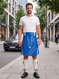 A man stands on a city sidewalk wearing a bright blue kilt with white geometric stripe details, a white t-shirt, white knee-high socks, and black leather shoes. Buildings, trees, a parked black car, and a bicycle are visible in the background.
