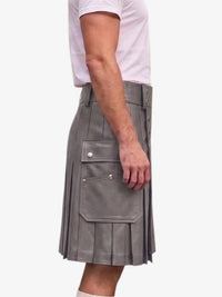 A side view of a person wearing a gray faux-leather kilt with pleats, flap pockets, and silver snap buttons, paired with a white t-shirt against a plain white background.