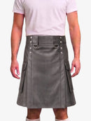 A man wearing a gray faux-leather kilt with silver-tone metal hardware, side pockets, and a belt loop, paired with a light pink t-shirt against a plain white background.